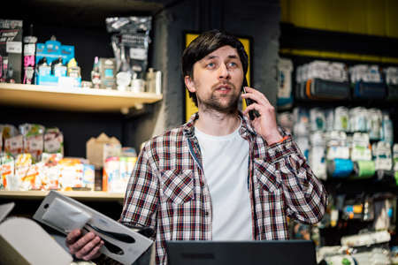 Bike shop owner at work. Store employee takes an order by mobile phone at table near laptop in travel and sporting goods store. Small business, communication, people and service concept.の写真素材