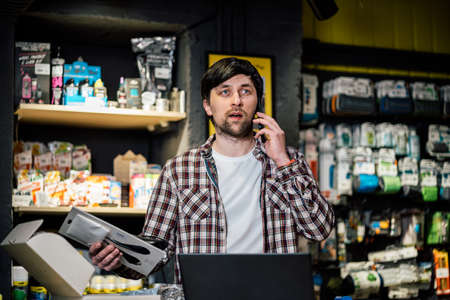 Small business owner on phone and computer in store. Sport shop worker making call with cell phone. Salesman working and talking on cell phone in bicycle shop. Seller taking orders by phone.の写真素材