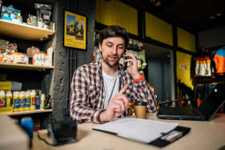 Small business owner on phone and computer in store. Sport shop worker making call with cell phone. Salesman working and talking on cell phone in bicycle shop. Seller taking orders by phone.の写真素材