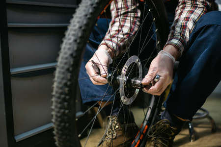 Technical expertise taking care bicycle shop. Handsome young mechanic fixing cycle wheel in workshop. Handsome repairman in workwear serving mountain bicycle. Male engineer adjusting velocipede.の写真素材