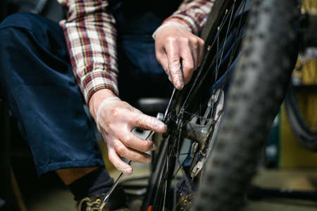 Young caucasian repairman repairing mountain bike wheel in bike shop workshop. Fixing bicycle. Caring for you wheels. man mechanic working in garage. Worker fixing cycle gear. Small business theme.の写真素材