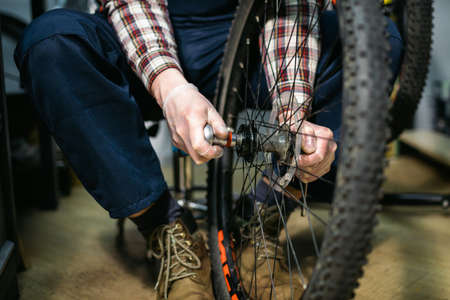 Bicycle mechanic fixing cycle wheel in repair shop. Velocipede service. Repairer male bike shop engineer fix bicycle wheel in workshop. Technician fixes bike parts. Handyman at work in the workplace.の写真素材