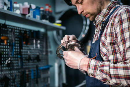 Bicycle mechanic fixing cycle wheel in repair shop. Velocipede service. Repairer male bike shop engineer fix bicycle wheel in workshop. Technician fixes bike parts. Handyman at work in the workplace.の写真素材