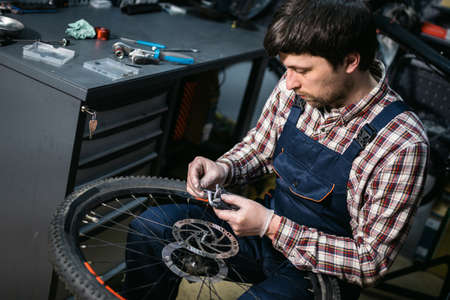 Young caucasian repairman repairing mountain bike wheel in bike shop workshop. Fixing bicycle....