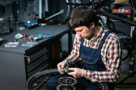 Bike shop mechanic fixing bicycle wheel in workshop. Serviceman repair, maintenance cycle. Velocipede repairing bicycle in bike shop. Bicycle repair service concept. Environmentally friendly vehicles.の写真素材