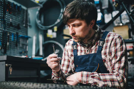 Bike shop mechanic fixing bicycle wheel in workshop. Serviceman repair, maintenance cycle. Velocipede repairing bicycle in bike shop. Bicycle repair service concept. Environmentally friendly vehicles.の写真素材