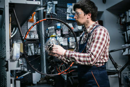 Bike shop mechanic fixing bicycle wheel in workshop. Serviceman repair, maintenance cycle. Velocipede repairing bicycle in bike shop. Bicycle repair service concept. Environmentally friendly vehicles.の写真素材