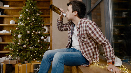 Problems of alcoholism in loneliness, sadness and melancholy during pandemic Male removes mask from virus, drinking wine from bottle during new year holidays sitting by Christmas treeの写真素材