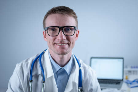 Happy confident male professional medic doctor close up portrait. Smiling doctor wear uniform looking at camera in office. Close-up of handsome German smile general practitioner wearing glassesの写真素材