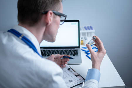 Scientist in medical laboratory examines vial of medicine, vaccine against viruses, influenza, covid. Doctor enters information into computer about investigation. Immunization from terrible diseasesの写真素材