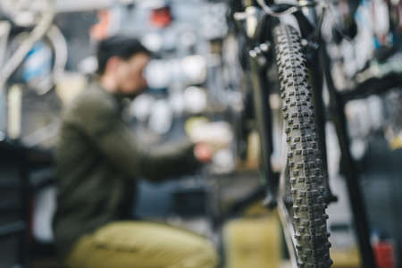 Mechanic repairs bicycle in workshop wearing covid 19 mask. Worker of bicycle store fixes bike during coronavirus quarantine in protective mask. Repairman maintenance cycle. Sport shop conceptの写真素材