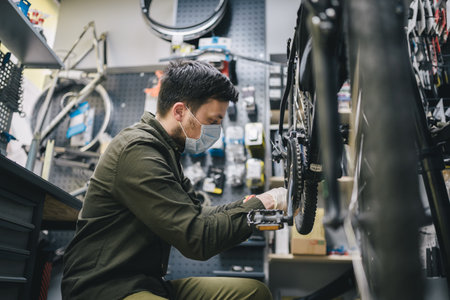 Bicycle mechanic wearing protective mask and gloves repairs customers bicycle wheel in accordance with quarantine standards during coronavirus pandemic. Small business during covid 19 lockdownの写真素材
