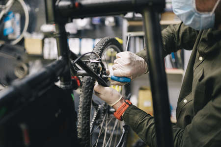 Bicycle mechanic wearing protective mask and gloves repairs customers bicycle wheel in accordance with quarantine standards during coronavirus pandemic. Small business during covid 19 lockdownの写真素材