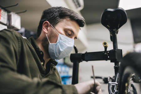 Bicycle shop repairman works in bicycle service and repair workshop during coronavirus quarantine...