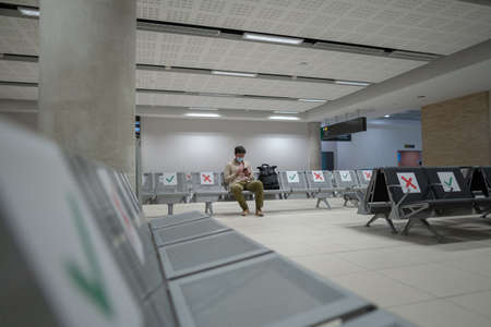 Waiting for flight at empty airport in Cyprus. Man sitting on chair with social distance marker at empty Paphos terminal. Flights canceled during quarantine.の写真素材
