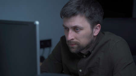 Tired male working on computer. Sad exhausted man at home office. Stressful work, stress at workplace. Software developer looks very tired during completion overtime of project, working on computerの写真素材