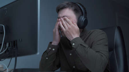 Home office. Handsome man working late at home. Tired young male feels pain, eye strain, dry...
