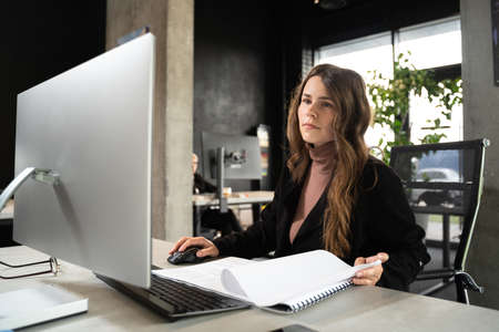 Design and architecture theme. A female young architect is working on a project with blueprints at the computer in a modern office. Architect engineer woman working plan at counting roomの写真素材