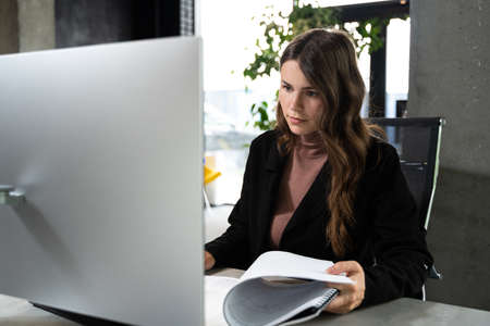 Design and architecture theme. A female young architect is working on a project with blueprints at the computer in a modern office. Architect engineer woman working plan at counting roomの写真素材