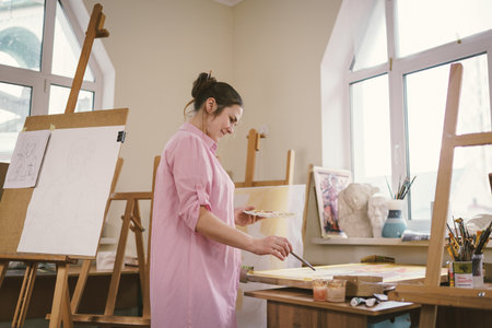 Female artist working in studio. Creative workspace, painting class, easel with canvas, art therapy. Inspiration, creativity, talent, craft concept. Artist studio interior. People, leisure and hobby.の写真素材