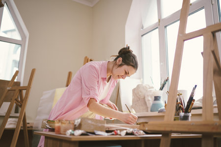 Female artist working in studio. Creative workspace, painting class, easel with canvas, art therapy. Inspiration, creativity, talent, craft concept. Artist studio interior. People, leisure and hobby.の写真素材