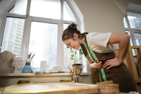 Caucasian woman artist working on a painting in bright daylight studio. Happy artist draws an art project with paints and a brush in the workshop. Hobby. Artist at work. Creative profession.の写真素材