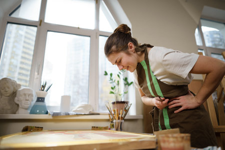 Cute woman paints on canvas in an art workshop. Artist creating picture. Art school or studio. Work with paints, brushes and easel. Hobby and leisure concept. Woman painter at workspace.の写真素材