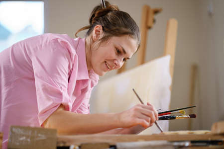 Female artist working in studio. Creative workspace, painting class, easel with canvas, art therapy. Inspiration, creativity, talent, craft concept. Artist studio interior. People, leisure and hobby.の写真素材