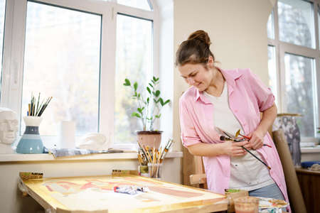 Female artist working in studio. Creative workspace, painting class, easel with canvas, art therapy. Inspiration, creativity, talent, craft concept. Artist studio interior. People, leisure and hobby.の写真素材