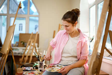 Art, creativity, hobby and creative occupation concept. Bringing creativity to life. Woman painting in art studio. Attractive female artist painting in workshop. Woman hobby, activity, profession.の写真素材
