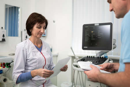 Doctor cardiologist in the office of ultrasound diagnostics with the patient examines medical tests during a health check-up in a modern clinic. Medical consultation. healthcare, medical service.の写真素材