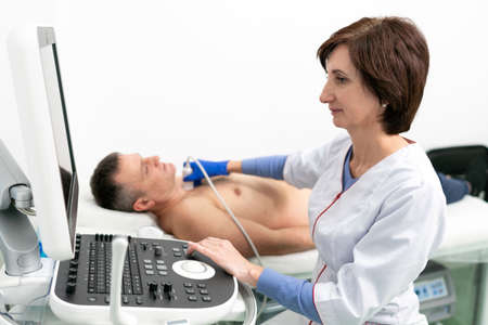 Doctor doing a doppler sonography a male patient in a cardiology clinic. Cardiologist performing an...