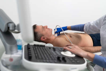 Doctor doing a doppler sonography a male patient in a cardiology clinic. Cardiologist performing an ultrasound examination at the cardiovascular hospital. Echocardiography procedure.の写真素材