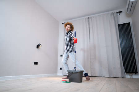 Jolly excited mature woman enjoying cleaning house, she dancing while washing floor. Happy elderly woman enjoying cleaning floors before moving to new apartment. Housework and housekeeping concept.の写真素材