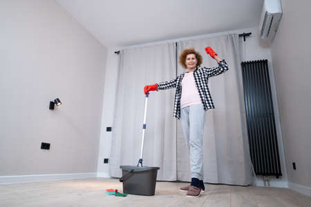 People, housework and housekeeping concept. Happy senior woman in protective gloves cleans floor and dances at home in empty apartment before moving to new home. Excited woman enjoying housekeeping.の写真素材
