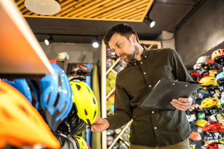 Bike shop manager checks helmet price information on tablet, seller makes an inventory in sports shop. Theme of small business selling bicycles. Seller in hands document checklist in bicycle store.の写真素材