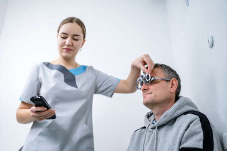 Examining patient vision. Eye exam. Optometrist checking patient eyesight and vision correction. Patient undergoing vision check with special ophthalmic glasses at eye clinic. Selection of eyeglasses.の写真素材