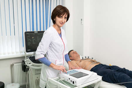 ECG concept. Woman doctor cardiologist doing electrocardiogram test to man patient in cardiology clinic. Medicine, cardiology, ECG of the heart concept. Male at medical testing.の写真素材