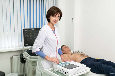 Cardiologist doctor performs electrocardiography procedure on man lying on couch in hospital. ECG test of male at modern clinic. Diagnostic, healthcare, medical service. Hospital patient and EKG test.の写真素材
