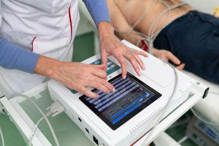 ECG concept. Woman doctor cardiologist doing electrocardiogram test to man patient in cardiology clinic. Medicine, cardiology, ECG of the heart concept. Male at medical testing.の写真素材