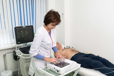 ECG concept. Woman doctor cardiologist doing electrocardiogram test to man patient in cardiology clinic. Medicine, cardiology, ECG of the heart concept. Male at medical testing.の写真素材