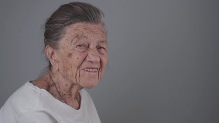 Senior woman 90 years old smiles, laughs and shows a denture on a gray background. Elderly female with deep wrinkles and gray hair happy in a good mood studio portrait looking at camera.の写真素材