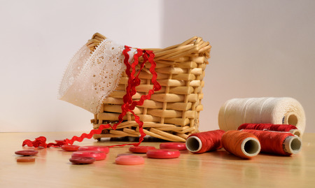 Sewing supplies, basket with laces, threads and buttons on wooden desk