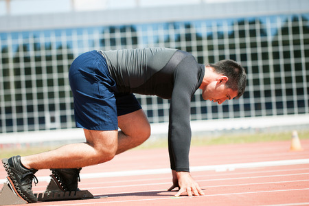 young muscular athlete is at the start of the treadmill at the stadium