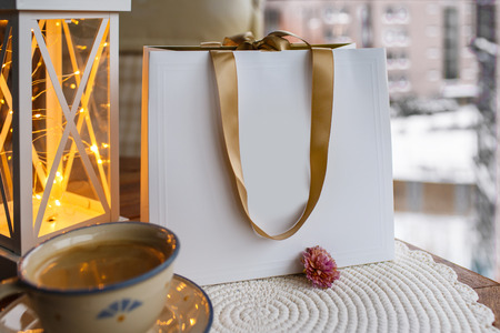 Mock up of blank craft package white paper shopping bag with Golden handles on a wooden table and cup of coffee Christmas mood.の写真素材