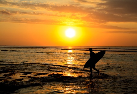 A surfer walking on the beach at sunsetの写真素材