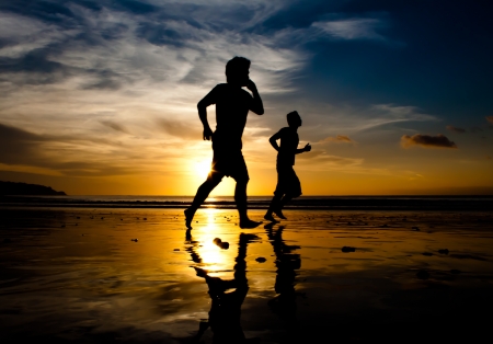 Two men running on Jimbaran beach at sunset with phoneの写真素材