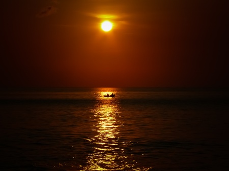 Small boat crossing the sun at sunset in Jimbaran Baliの写真素材