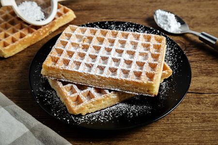 Sugar waffles presented on a black plate and over a wooden board