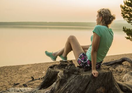a girl is sitting in a tree near the lakeの写真素材